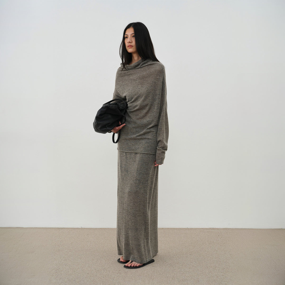 Brown cowl neck sweater and long skirt set, three-quarter front view on model holding a black bag