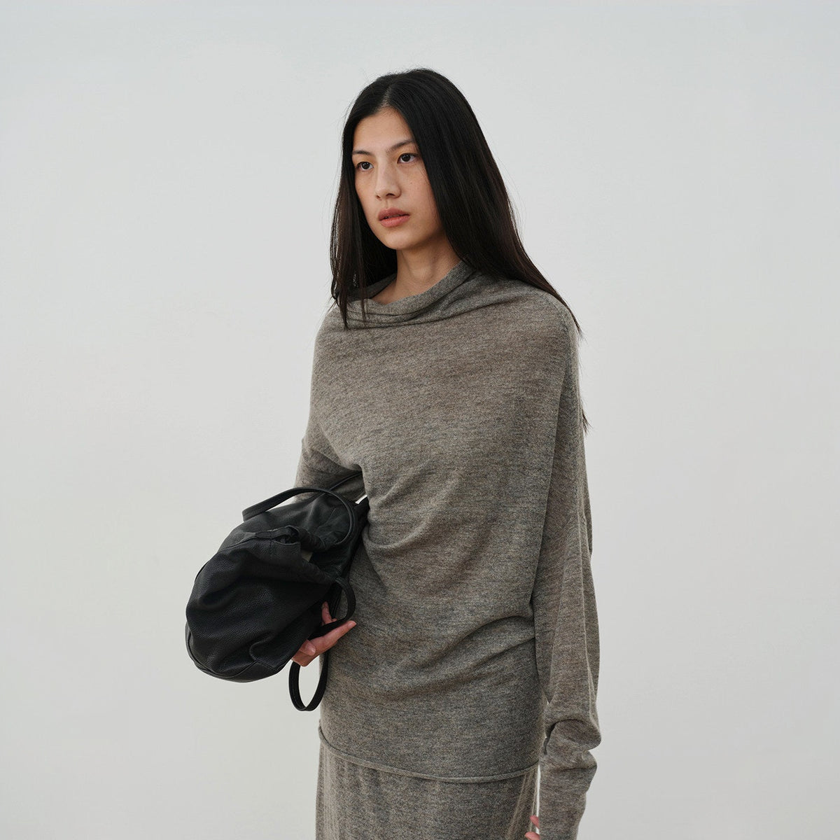 Brown cowl neck sweater with a draped neckline and raw hem, close view on model
