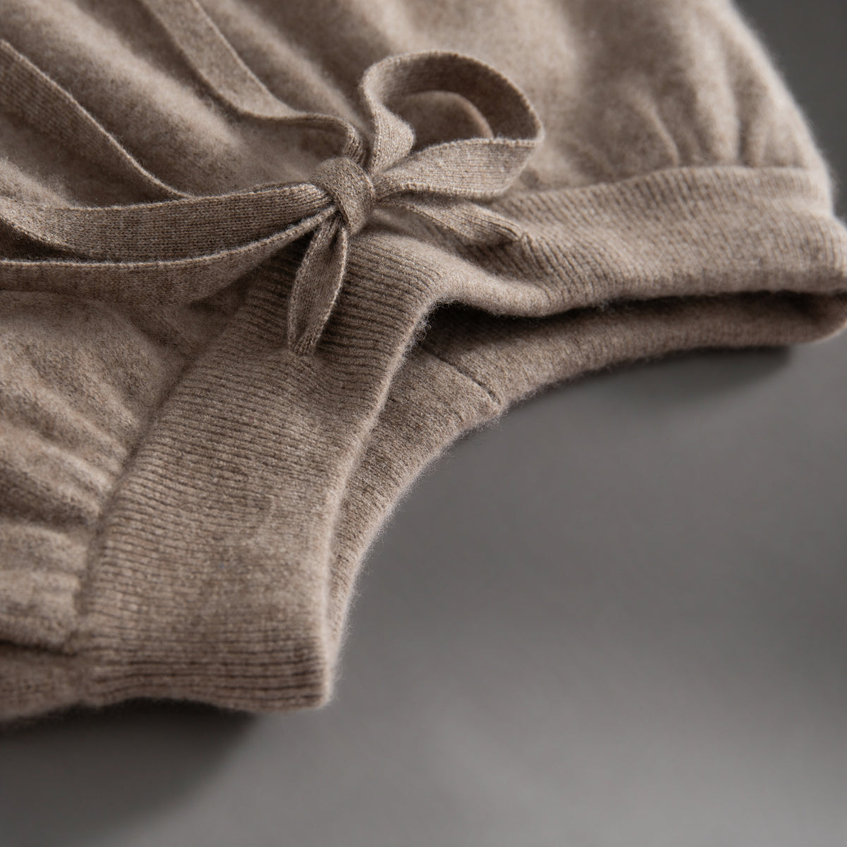 Cashmere drawstring trousers in brown, waist and drawstring detail, on a grey studio backdrop