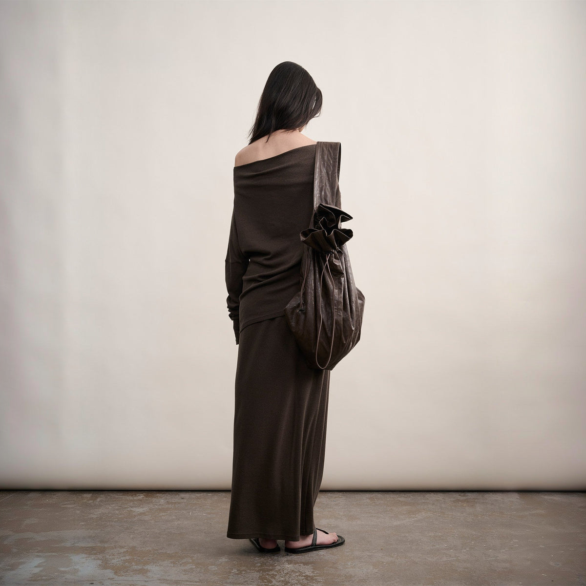 Brown cotton one-shoulder top and skirt set, full-length back view on model with a drawstring bag on the shoulder