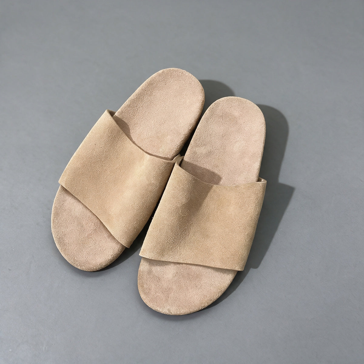 Matte cowhide slide sandals in pale beige, on a grey studio backdrop
