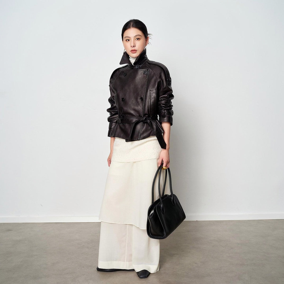 Vegetable-tanned sheepskin leather jacket in black, worn belted over cream, full length