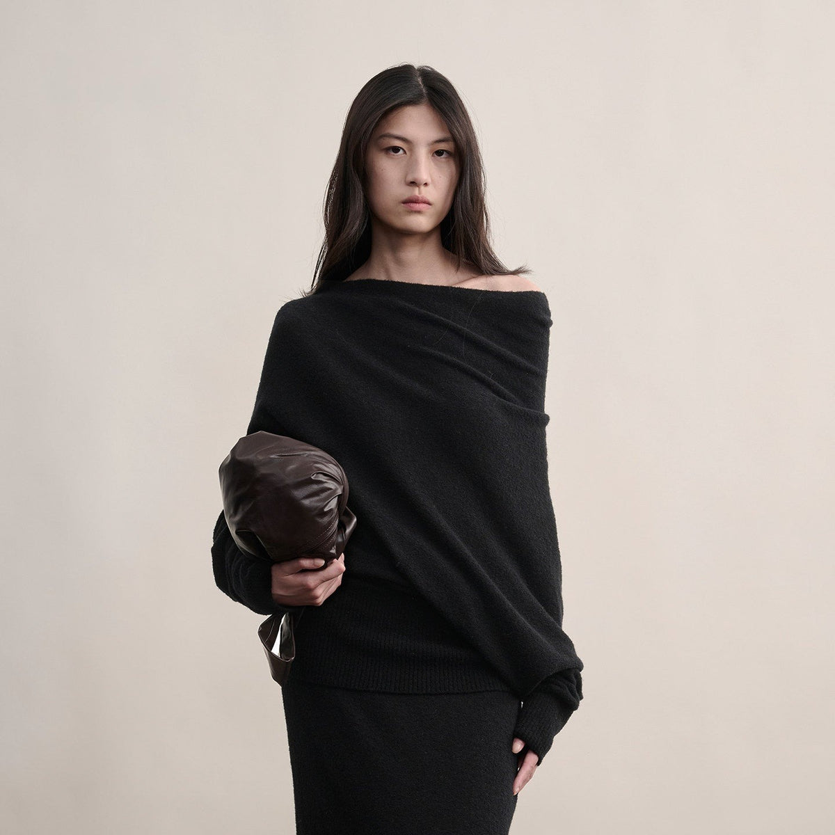 Black off-shoulder wool sweater, upper-body view on model holding a clutch