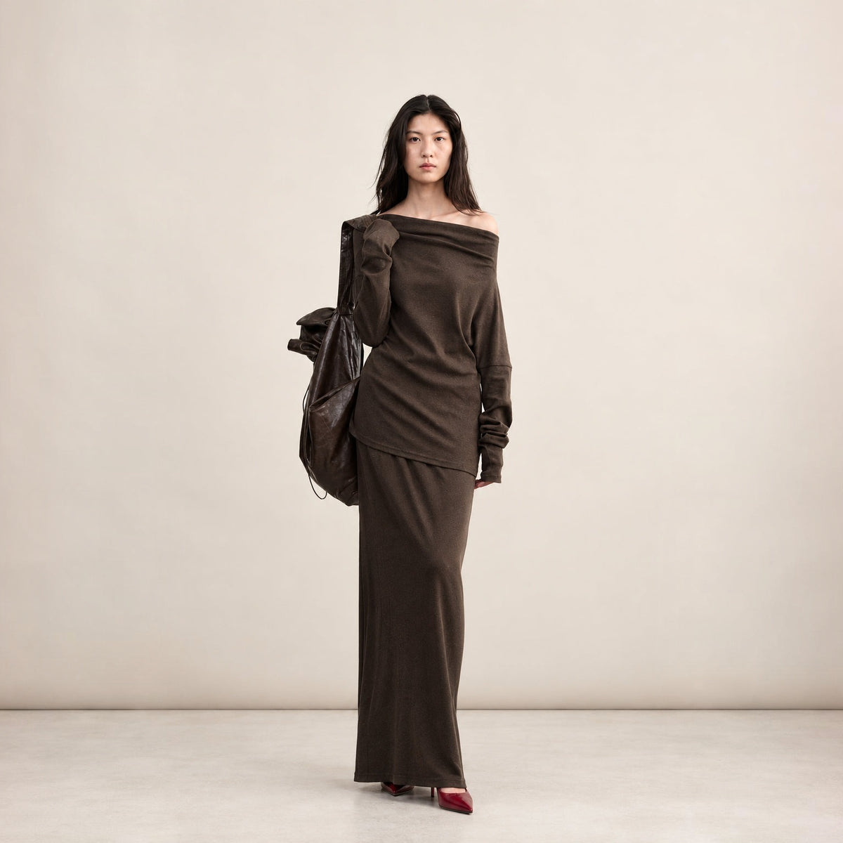 Brown cotton one-shoulder top and skirt set, full-length front view on model carrying a drawstring bag