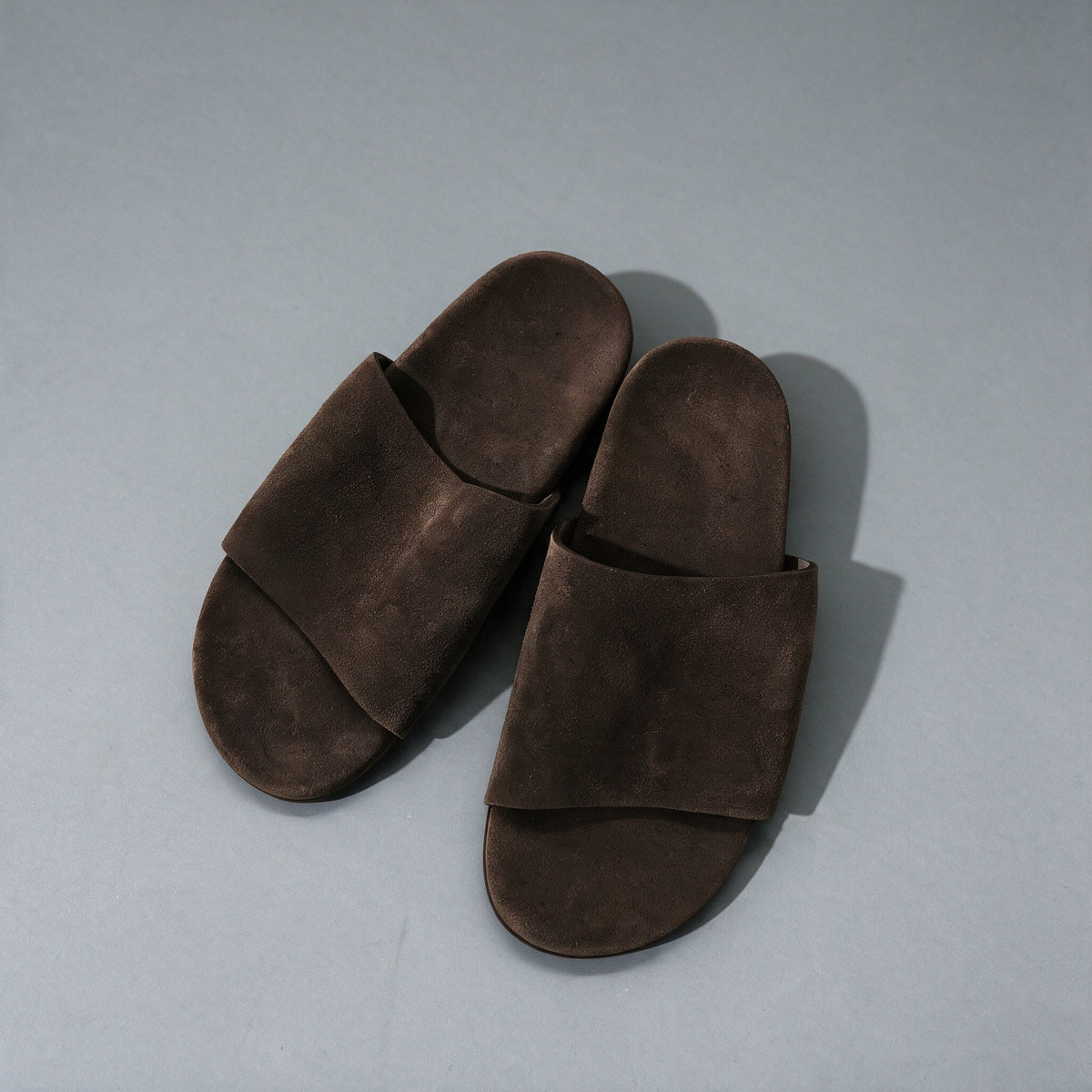 Matte cowhide slide sandals in dark brown, on a grey studio backdrop