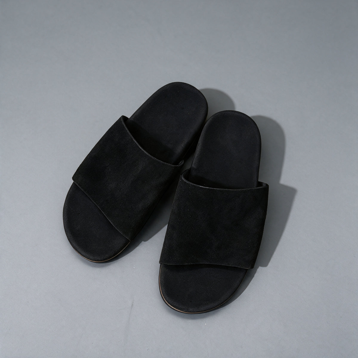Matte cowhide slide sandals in black, on a grey studio backdrop