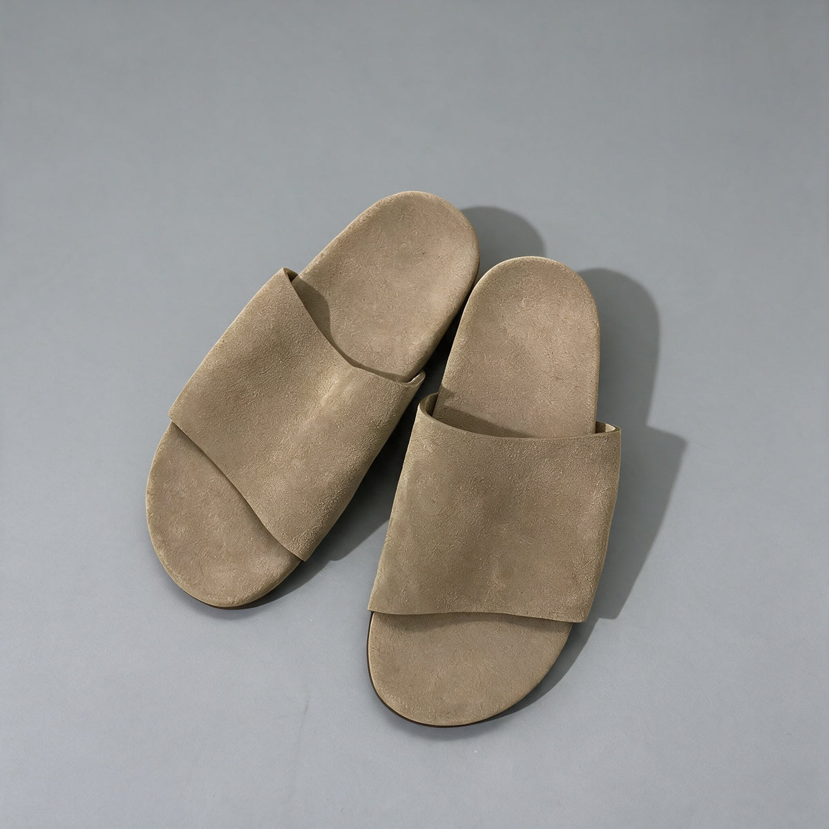 Matte cowhide slide sandals in taupe brown, on a grey studio backdrop