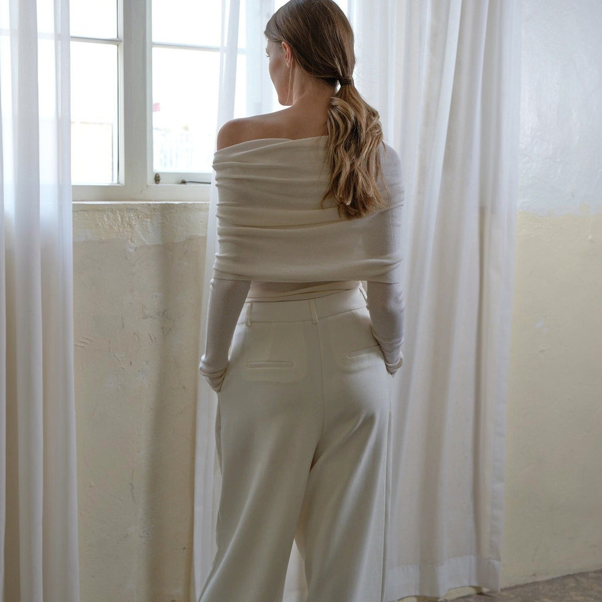 Off shoulder sweater in white, back view with the folded neckline across the shoulders and a low ponytail