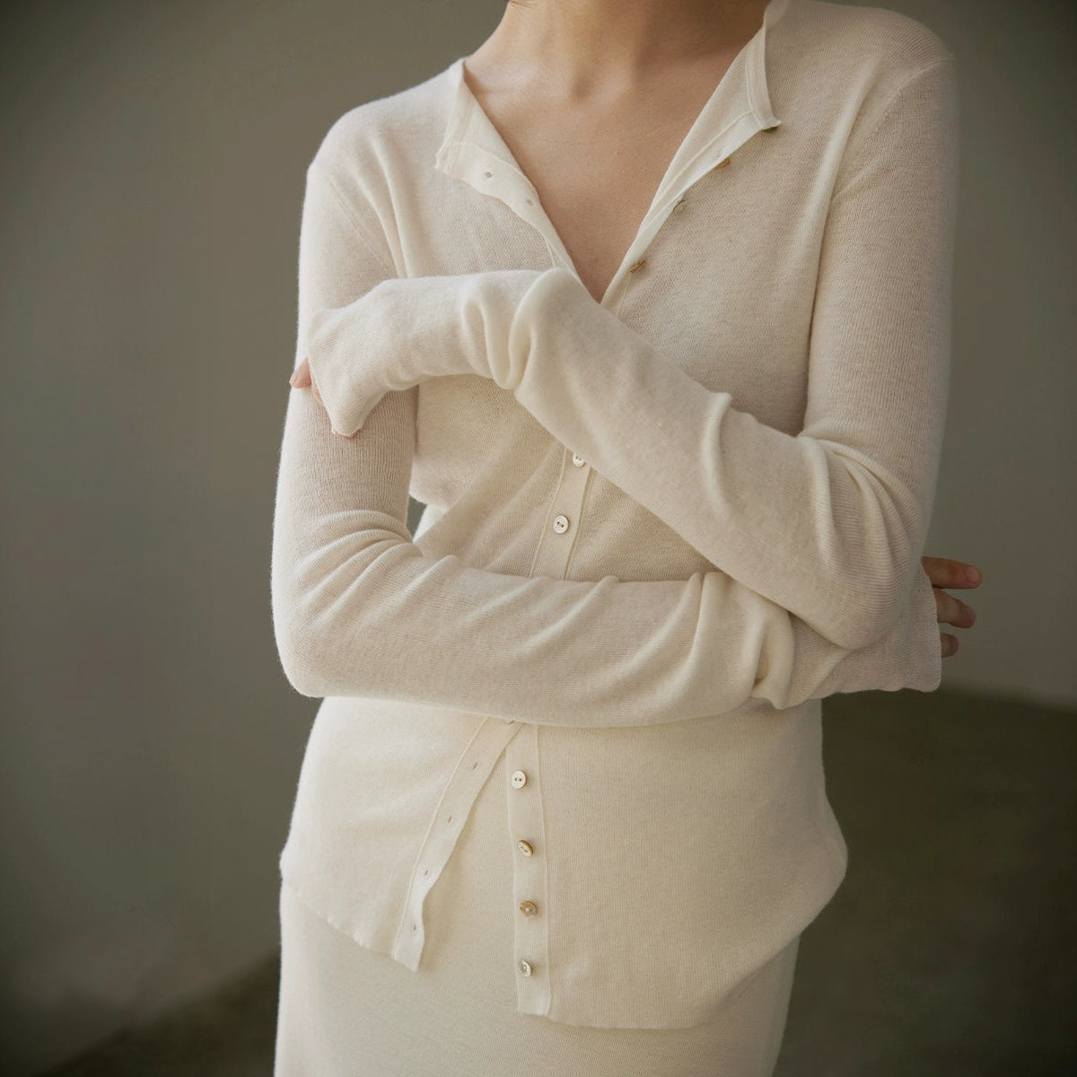 Sheer fine-knit wool cardigan in cream, buttons down the front, close crop with arms crossed