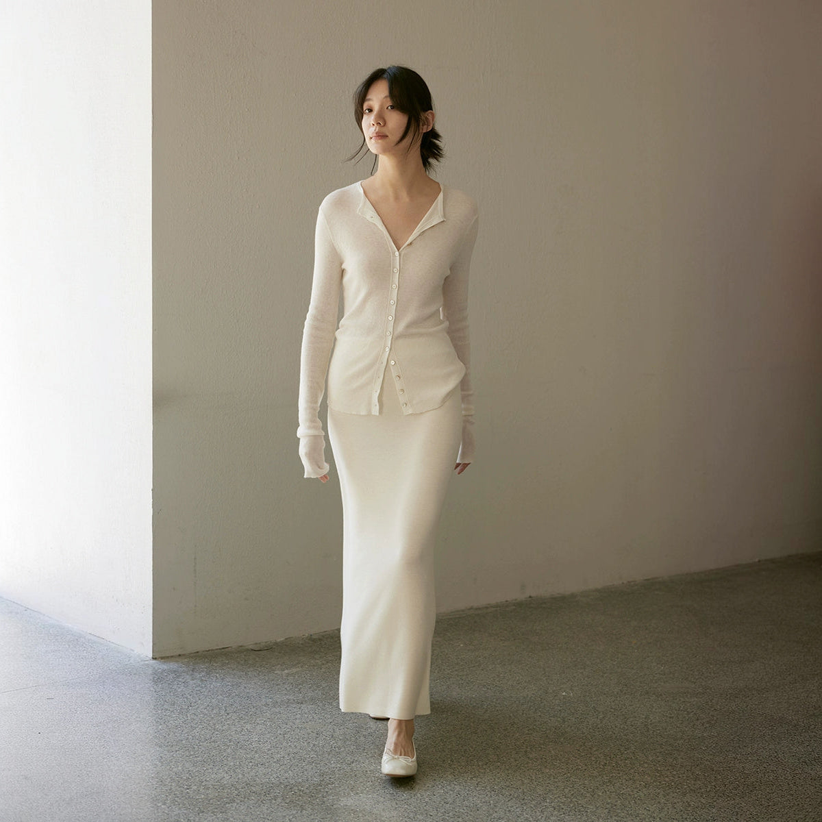 Cardigan over a long skirt, both in cream, full length walking on a grey floor
