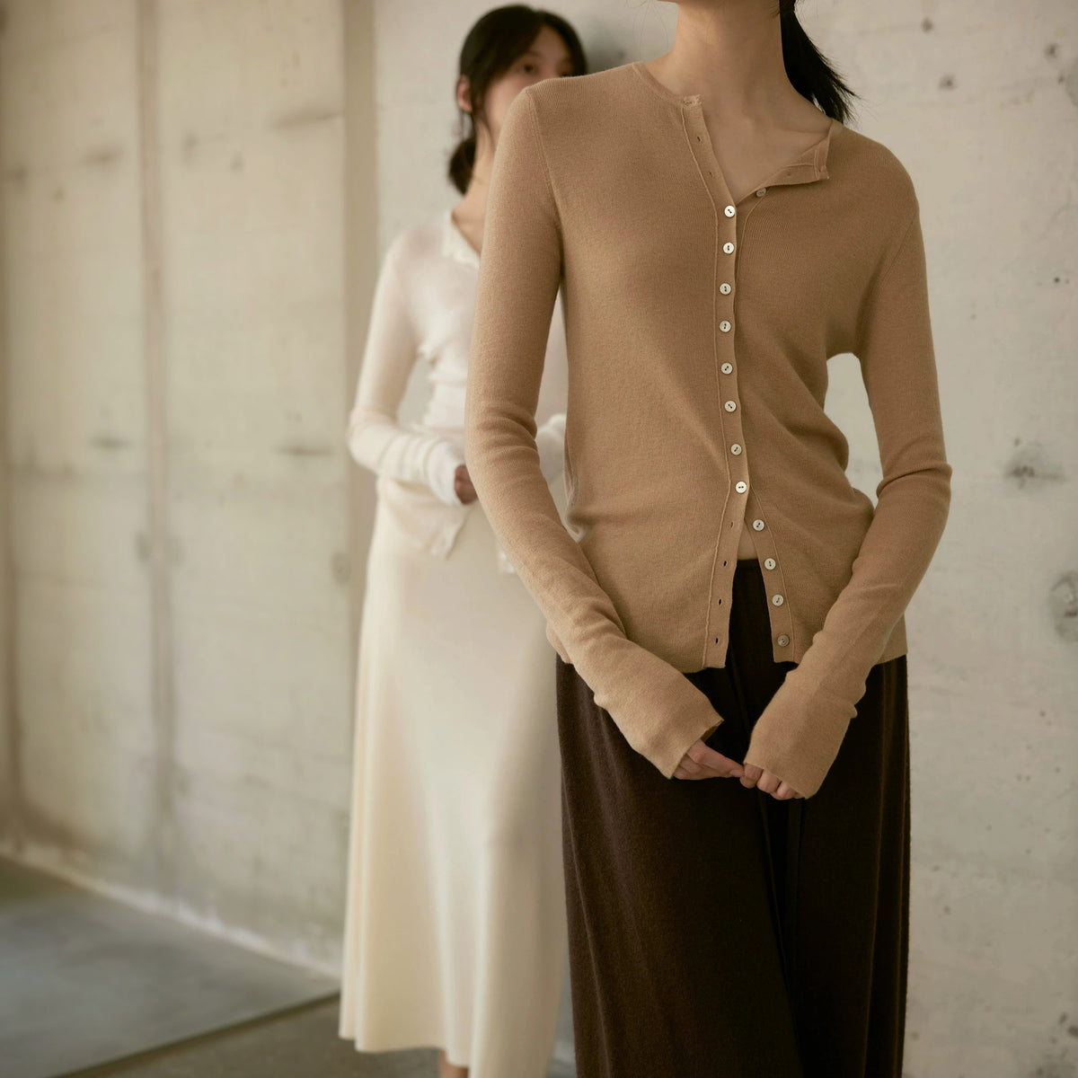 Fine-knit wool cardigan in tan, torso crop of the buttons and hands, a second model in cream behind