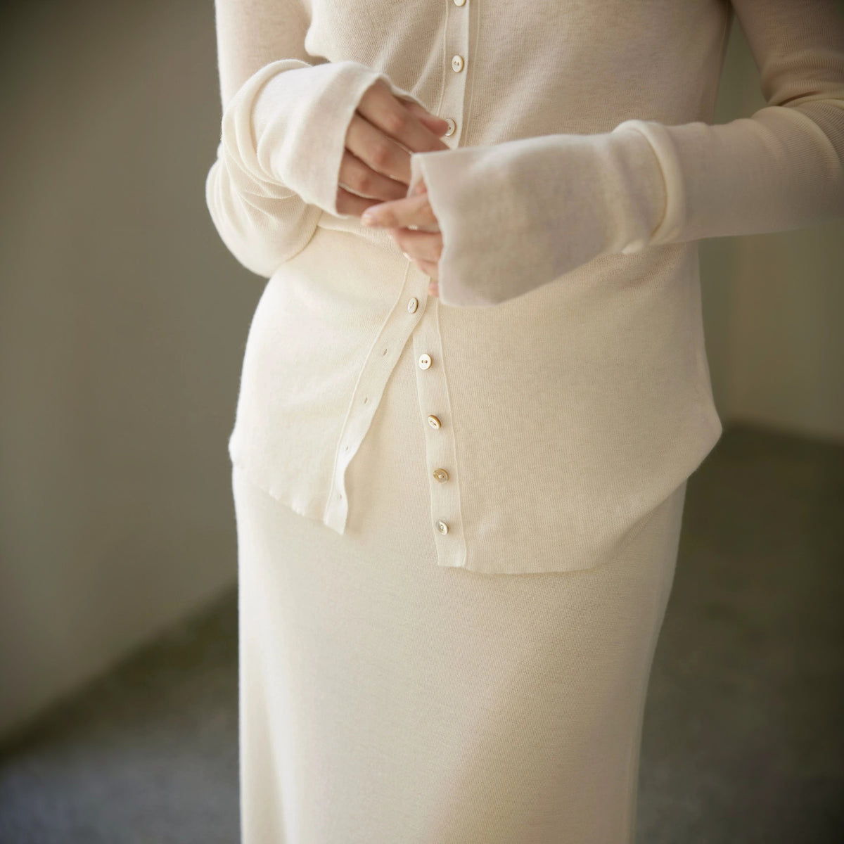 Sheer wool cardigan in cream, close crop of the buttons, cuff and waist with hands in frame
