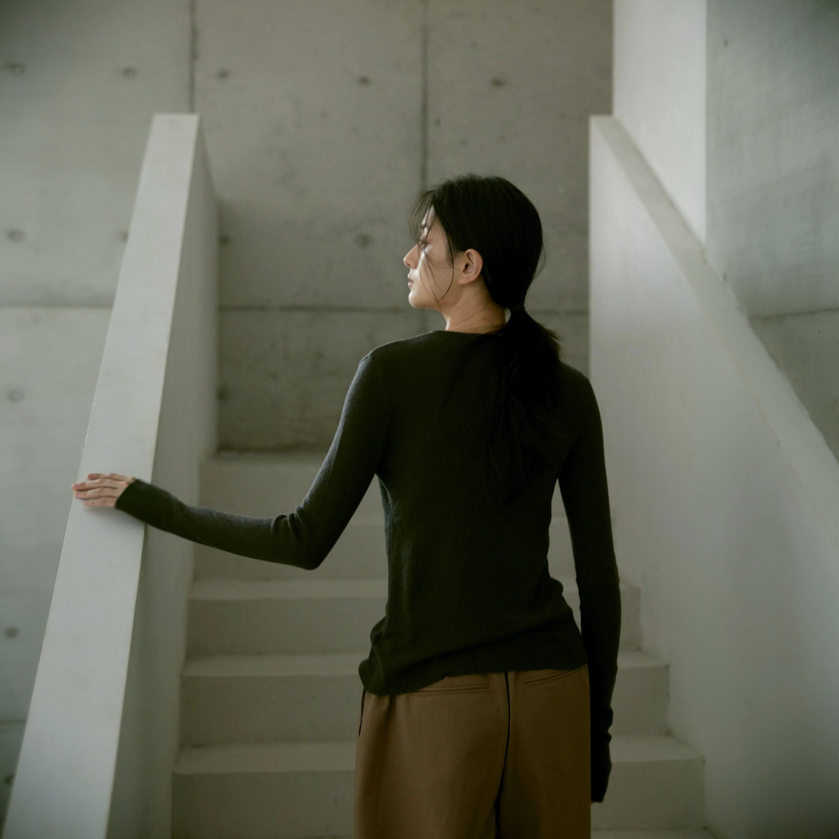 Wool cardigan in dark olive, back view on a stairway with a hand on the rail