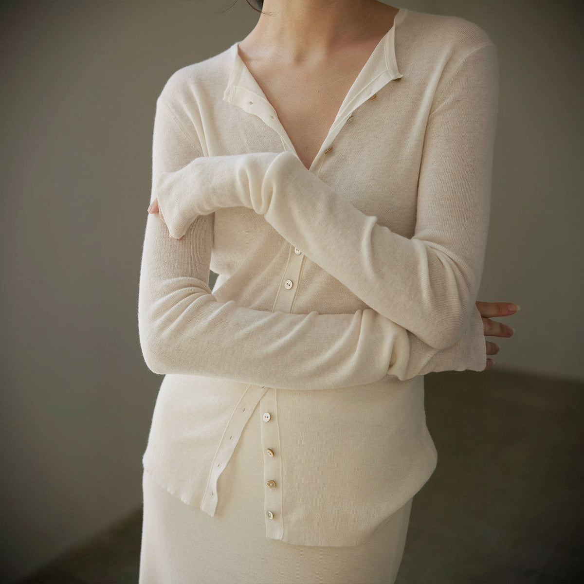 Sheer wool cardigan in cream, torso crop with crossed arms on a square frame