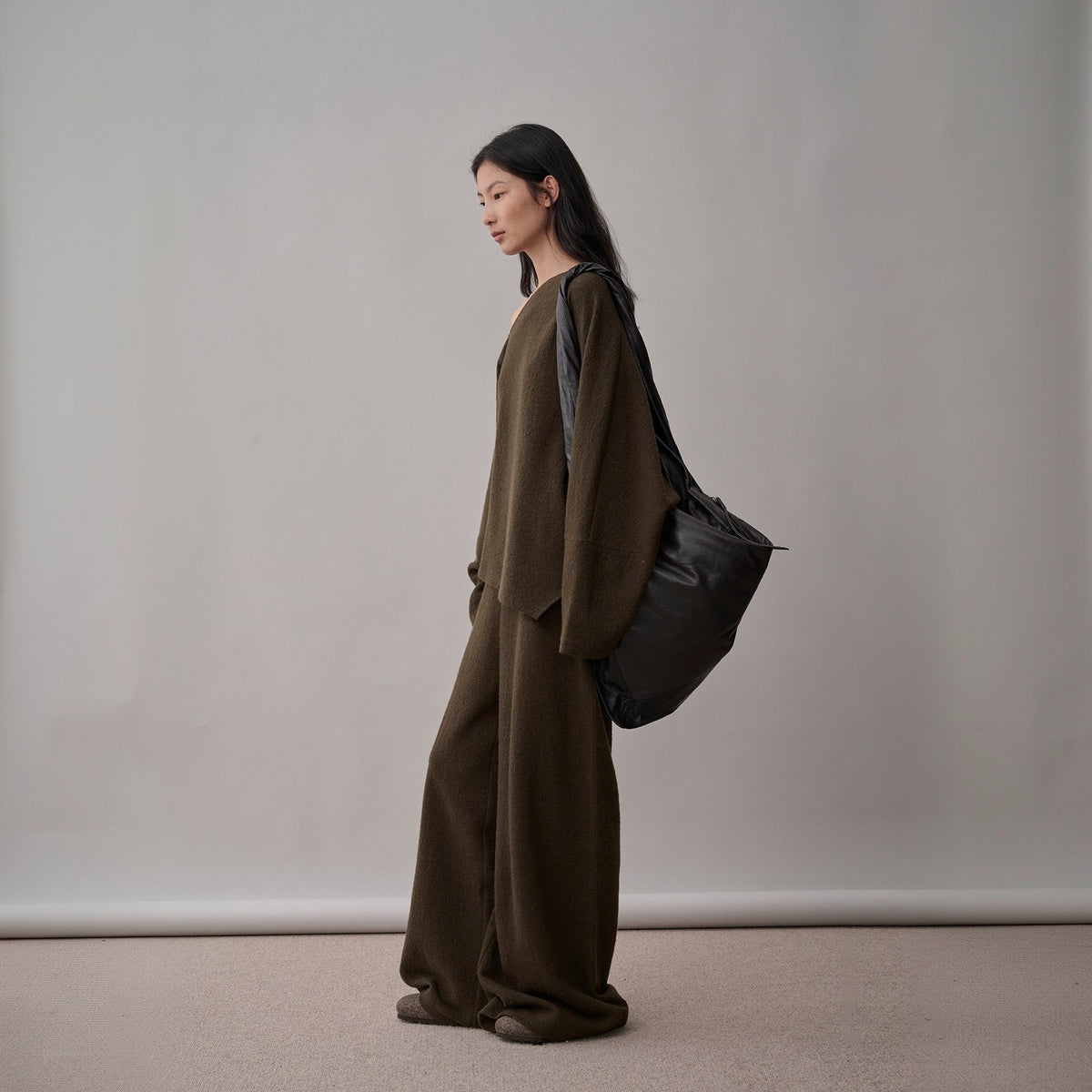 Dark brown wool sweater and wide-leg pants set, side view on model with a black bag on the shoulder