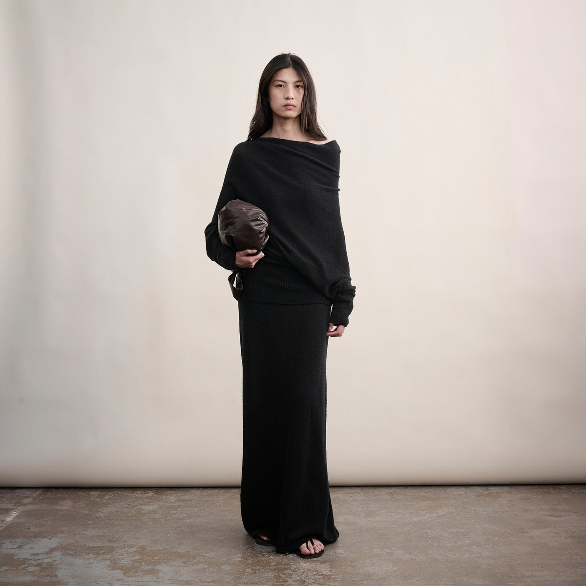 Black off-shoulder wool sweater and long skirt set, full-length front view on model holding a clutch